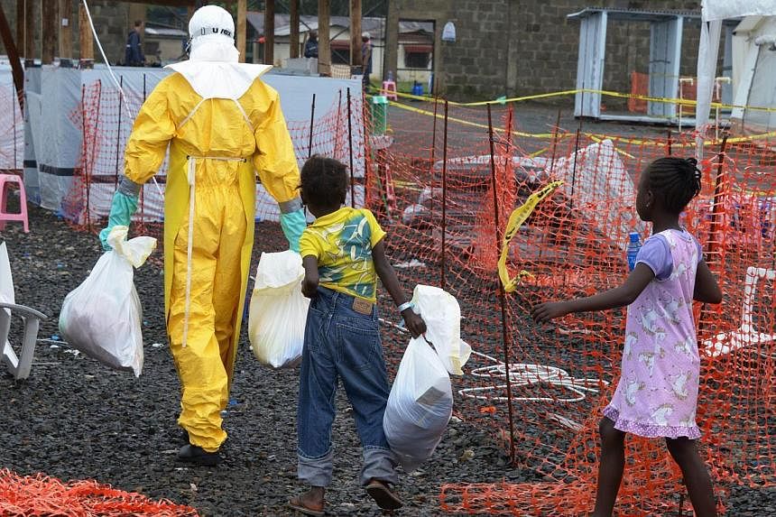 A medical worker wearing a protective suit carries bags followed by Ebola infected children in the high-risk area of the Elwa hospital runned by Medecins Sans Frontieres (Doctors without Borders) in Monrovia, on Sept 7, 2014. &nbsp;-- PHOTO: AFP