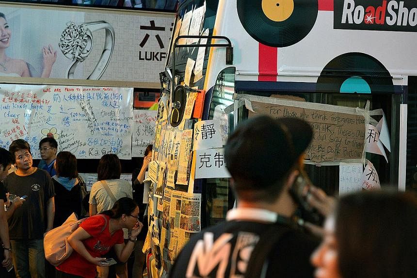 Passersby take pictures of messages and cartoons pasted the windscreen of buses stranded in the protest area at Mong Kok in Kowloon on 1 Oct 2014, during the protests.&nbsp;Beijing has pledged its support for Hong Kong's embattled leader Leung Chun-y