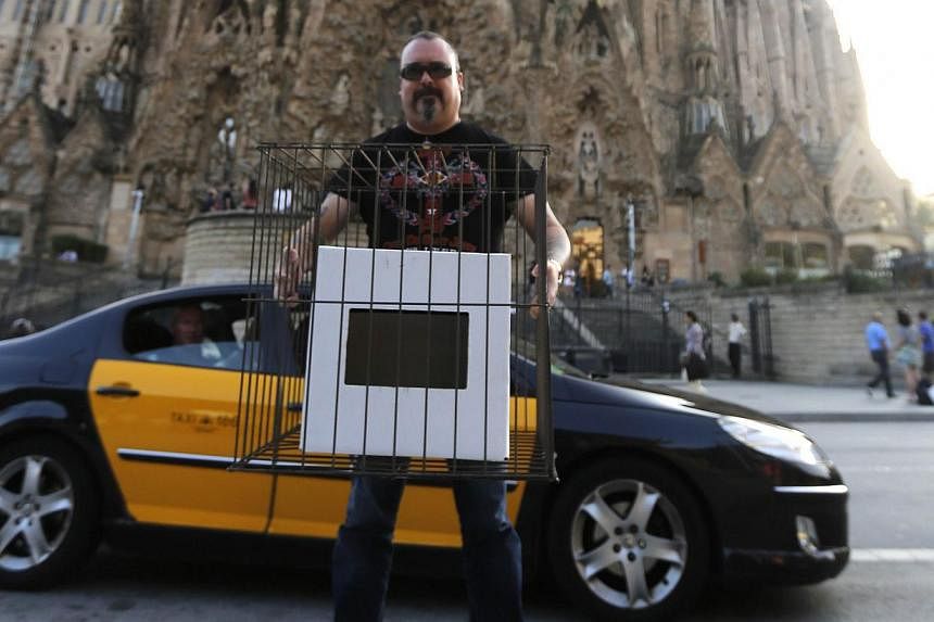 A member of Catalan pro-independence supporter group "Muts i a la Gabia" (Silenced and Caged) holds a ballot box fitted in a cage during a protest against the Spanish Constitutional Court in front of the Basilicia Sagrada Familia in Barcelona on Oct 