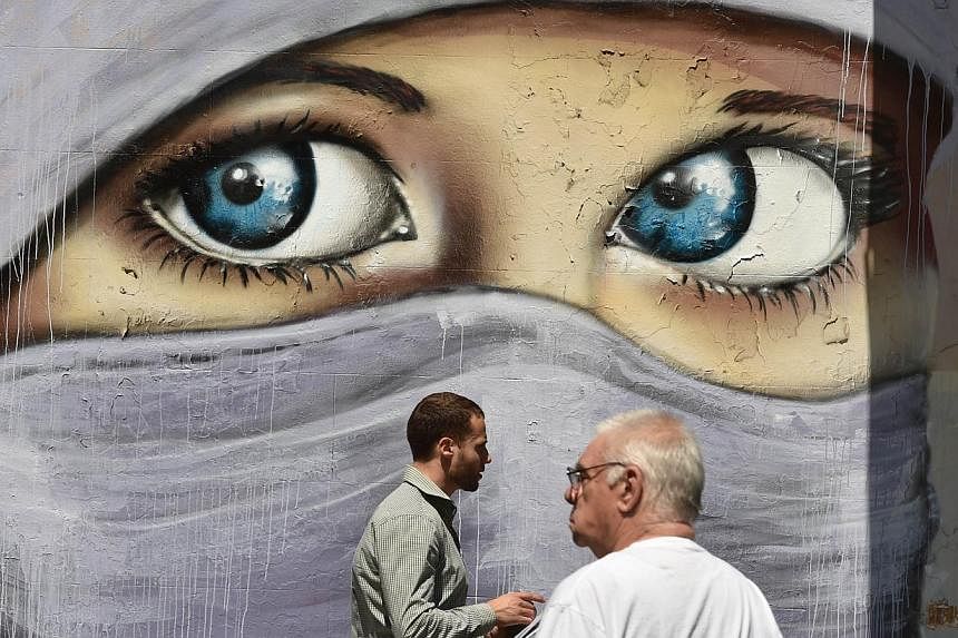 People walk past a mural of a Muslim woman painted on a wall in an inner city suburb in Sydney on Oct 2, 2014. Australian Prime Minister Tony Abbott asked officials to re-think restrictions on members of the public wearing face-coverings such as burq