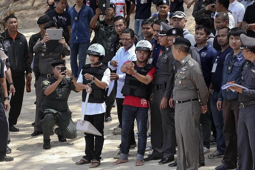 Two workers from Myanmar (wearing helmets and handcuffs), suspected of killing two British tourists on the island of Koh Tao last month, stand near Thai police officers during a re-enactment of the alleged crime, where the bodies of the tourists were