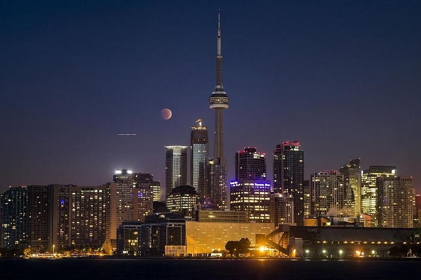 The moon turns orange during a total lunar eclipse behind the CN Tower and the skyline during moonset in Toronto on Oct 8, 2014.&nbsp;-- PHOTO: REUTERS