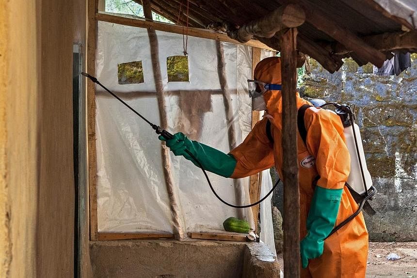 A volunteer in protective suit sprays disinfectant outside a home in Waterloo, Sierra Leone, on Oct 7, 2014, prior to taking away the body of a woman who died of Ebola.&nbsp;The epidemic could deal a US$32.6 billion (S$41 billion) blow to the West Af