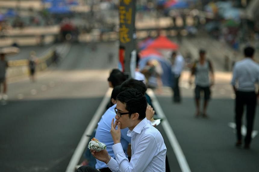 Office workers tainge their lunch sitting on a road divider in an area blocked off by protesters of the Occupy Central movement. -- ST PHOTO: &nbsp;KUA CHEE SIONG