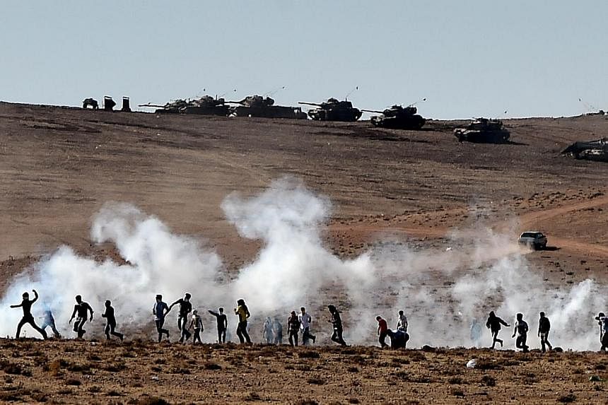 Kurdish people throw stones at Turkish armoured vehicles firing tear gas as Turkish army soldiers try to remove people from the Turkish-Syrian border area near the Syrian town of Ain al-Arab, known as Kobane by the Kurds, in the southeastern town of 
