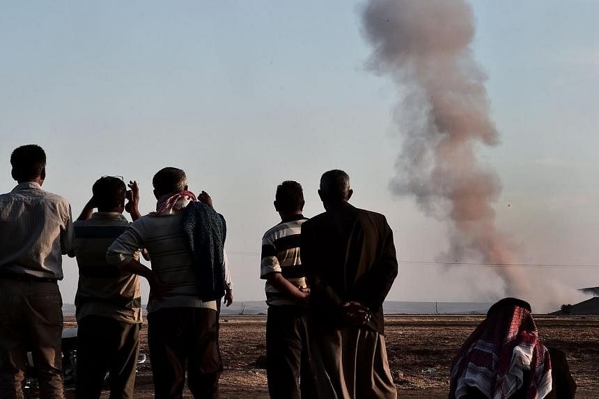 People watch smoke rising from the Syrian town of Ain al-Arab, known as Kobane by the Kurds, after an air strike, on Oct 8, 2014 in the Turkish-Syrian border, in the south-eastern village of Mursitpinar, Sanliurfa province. -- PHOTO: AFP