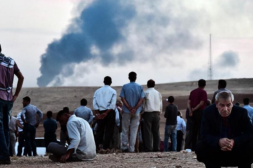 Kurdish people stand on a hill at the Turkish-Syrian border as smoke rises from the Syrian town of Ain al-Arab, known as Kobane by the Kurds, in the southeastern village of Mursitpinar, Sanliurfa province, on Oct 9, 2014.&nbsp;Islamic State group mil