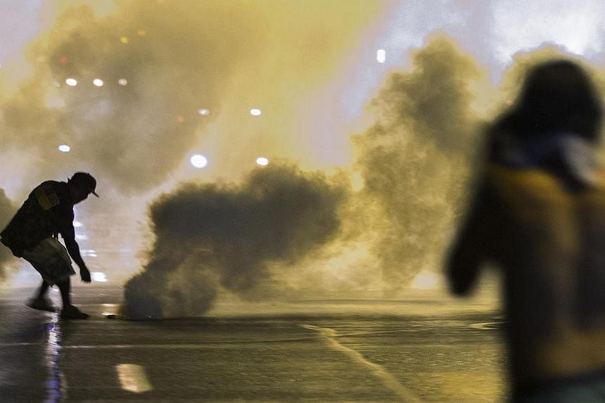 A protester reaches down to throw back a smoke canister as police clear a street after the passing of a midnight curfew meant to stem ongoing demonstrations in reaction to the shooting of Michael Brown in Ferguson, Missouri on Aug 17, 2014.&nbsp;An i