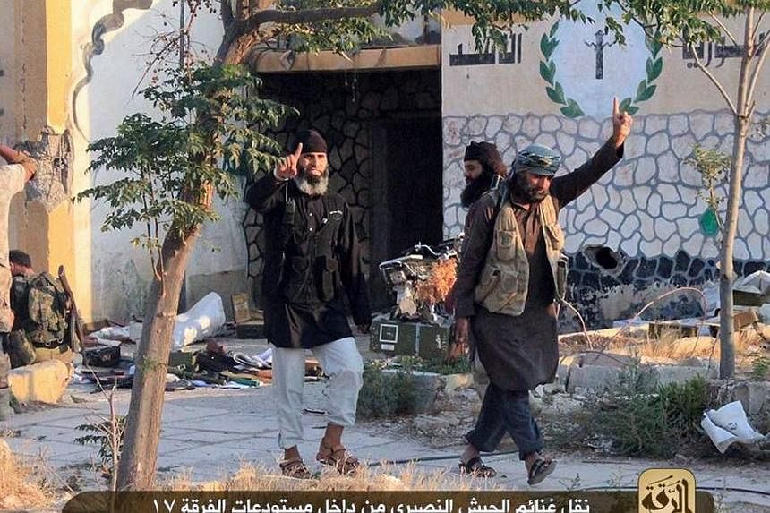 An image made available by militant media outlet Welayat Raqa on July 25, 2014, allegedly shows members of the Islamic State extremist group raising their index fingers, as they loot ammunition from a Syrian army base in the northern rebel-held Syria
