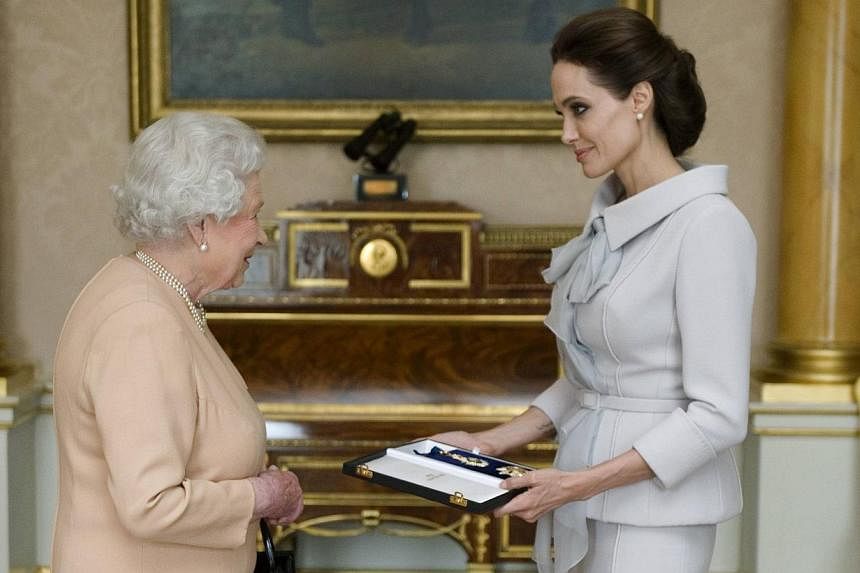 Actress Angelina Jolie is presented with the Insignia of an Honorary Dame Grand Cross of the Most Distinguished Order of St Michael and St George, by Britain's Queen Elizabeth II in the 1844 room at Buckingham Palace in London on October 10, 2014. --