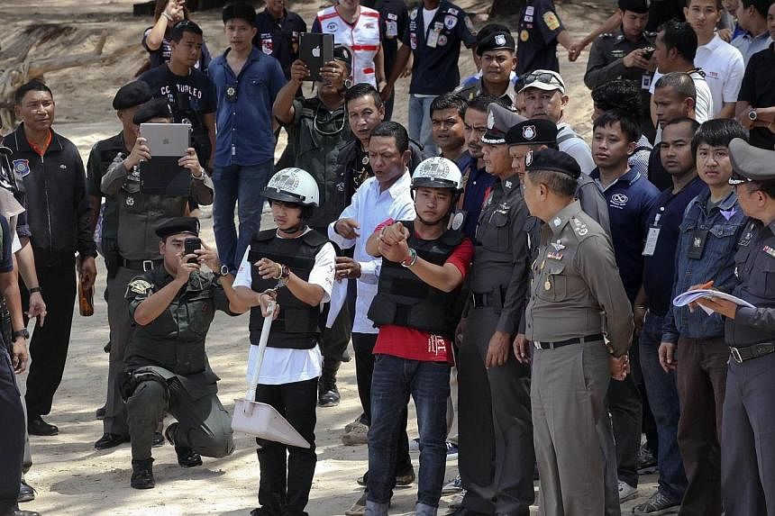 Two workers from Myanmar (wearing helmets and handcuffs), suspected of killing two British tourists on Koh Tao last month, stand near Thai police officers during a re-enactment of the alleged crime on Oct 3, 2014.&nbsp;The lawyers of the two men have