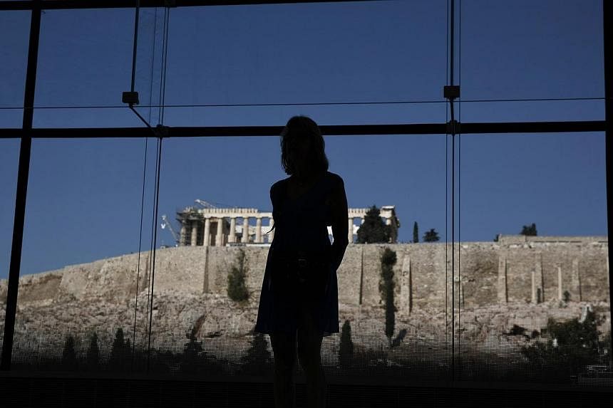 A woman looks at exhibits on display in the Parthenon hall at the Acropolis museum, as the temple of the Parthenon is seen in the background, in Athens, Greece on Oct 10, 2014. -- PHOTO: REUTERS