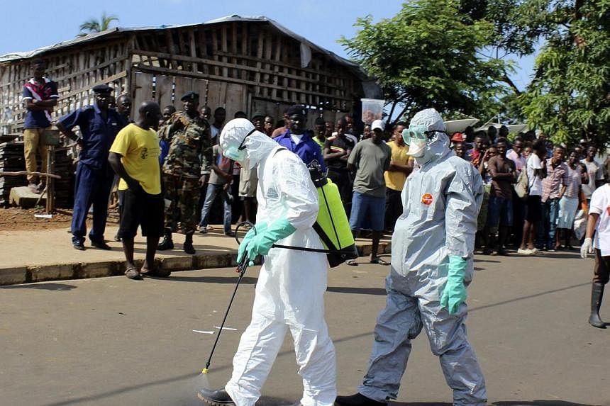 Health workers spray themselves with chlorine disinfectants after removing the body a woman who died of Ebola virus in the Aberdeen district of Freetown, Sierra Leone on Oct 14, 2014.&nbsp;-- PHOTO: REUTERS