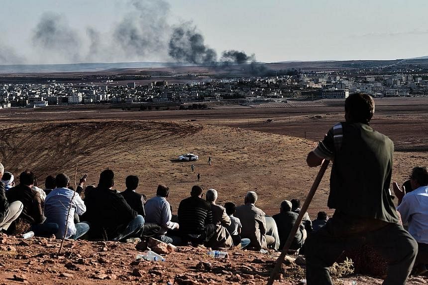 Kurdish people watch smoke billowing from Kobane as they gather upon a hill overlooking the Syrian town of Kobane, also known as Ain al-Arab, in the southeastern village of Mursitpinar, Sanliurfa province, on Oct 15, 2014. US-led airstrikes have kill