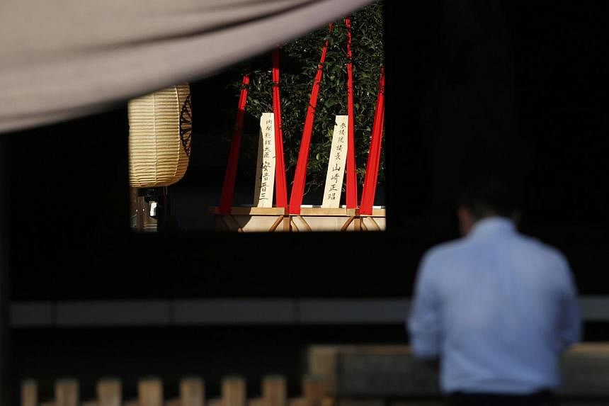 A wooden sign (left) which reads "Prime Minister Shinzo Abe" is seen on a ritual offering, a masakaki tree, from the prime minister to the Yasukuni Shrine, inside the main shrine as a visitor prays at the front shrine in Tokyo, Japan on Oct 17, 2014.
