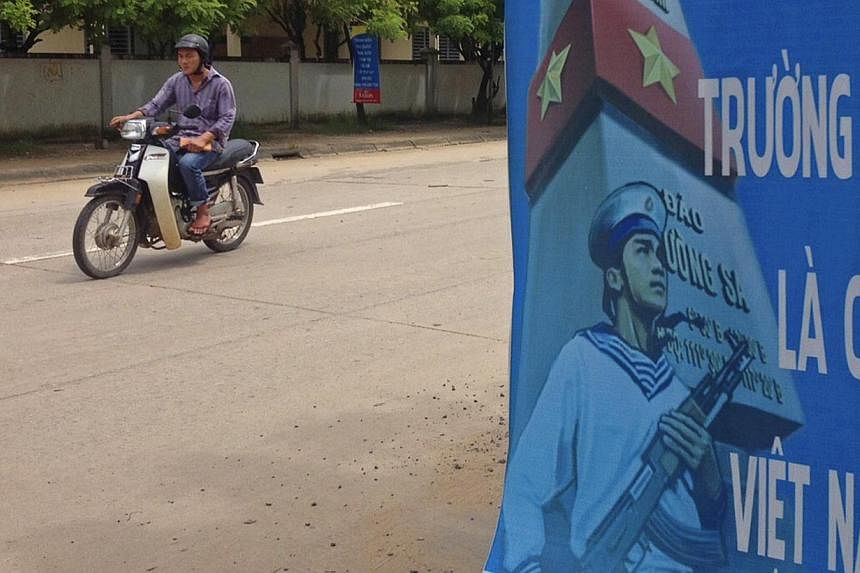 A man riding a motorcycle past a poster promoting Vietnam' sovereignty in what is calls the East Sea (also known as the South China Sea) on Phu Quoc island Sept 11, 2014. The poster reads: "Paracel Islands, Spratly Islands belong to Vietnam". -- PHOT