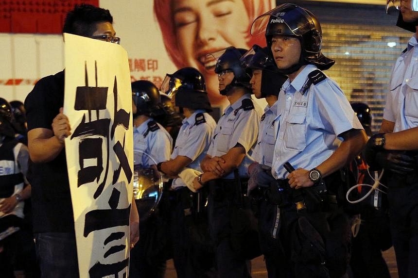 A pro-democracy protester carrying a banner which reads "black cop" in front of a line of policemen off a road blocked by pro-democracy protesters at Mongkok shopping district in Hong Kong on early October 17, 2014. -- PHOTO: REUTERS