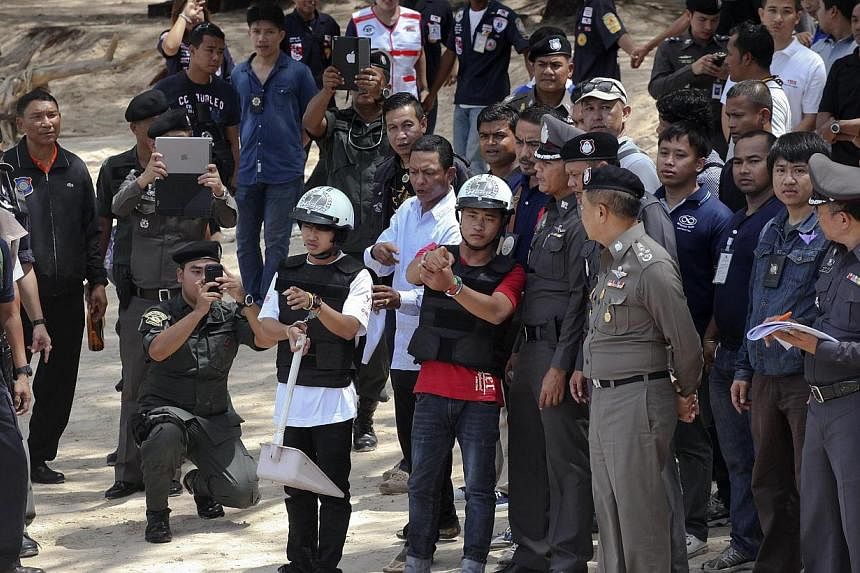 Two workers from Myanmar (wearing helmets and handcuffs), suspected of killing two British tourists on the island of Koh Tao last month, during a re-enactment of the alleged crime on Oct 3, 2014. Thailand's Prime Minister Prayuth Chan-O-Cha has agree