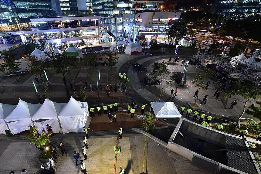 Policemen stand guard near a broken ventilation grate (right-bottom) after concert goers fell through it into an underground parking area below in Seongnam City, south of Seoul, on Oct 17, 2014.&nbsp;-- PHOTO: AFP