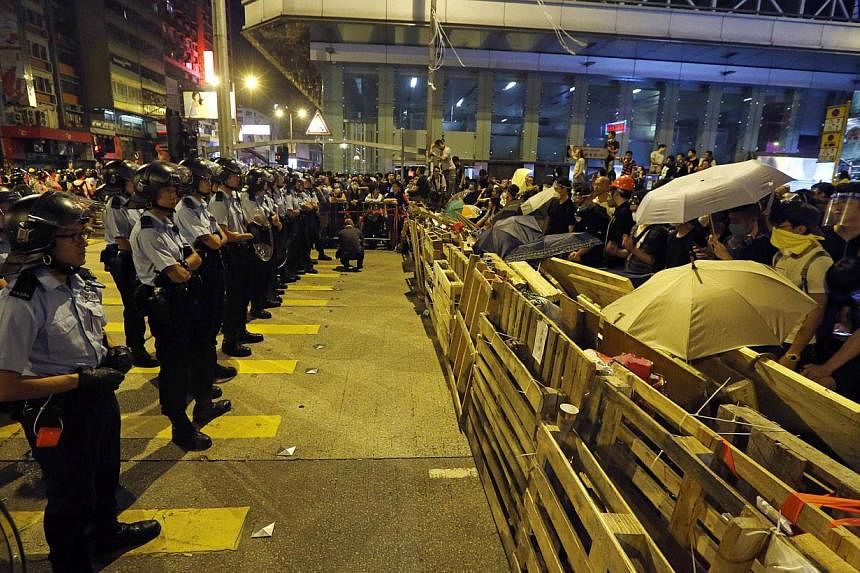 Riot police line up in front of protesters behind a barricade in the Mongkok shopping district of Hong Kong early Oct 19, 2014.&nbsp;Violent clashes erupted early on Sunday in a Hong Kong protest hotspot as unarmed pro-democracy activists once again 