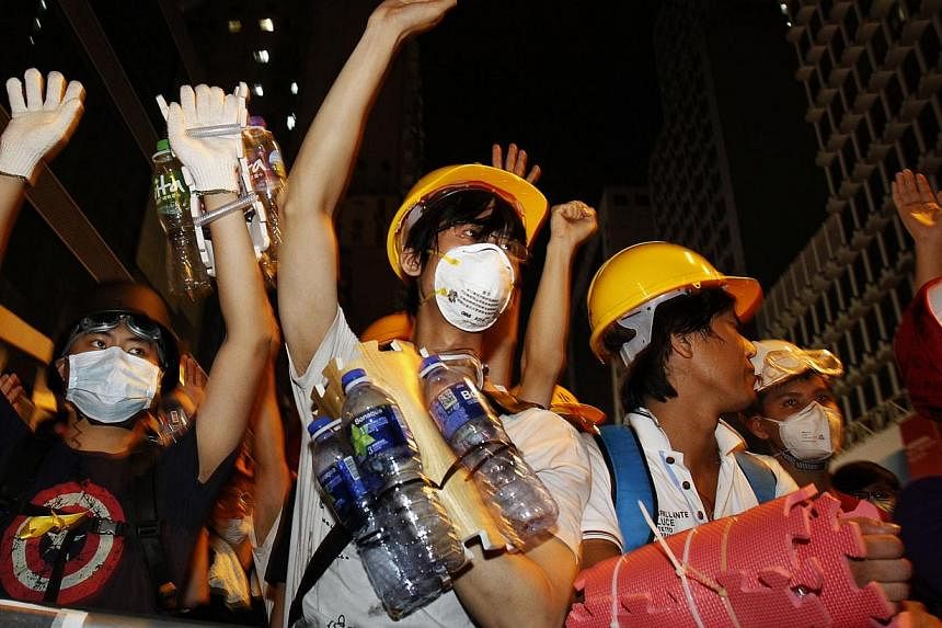 Pro-democracy protesters, protecting themselves with helmets, masks, foam pads and empty plastic bottles, raise their hands at riot police as a gesture of peace after they were told by visiting lawmakers not to charge the police defence line, at Mong