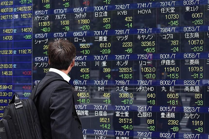 A pedestrian watches a share prices board displayed on a window of a securities firm in Tokyo on Oct 16, 2014. -- PHOTO: AFP