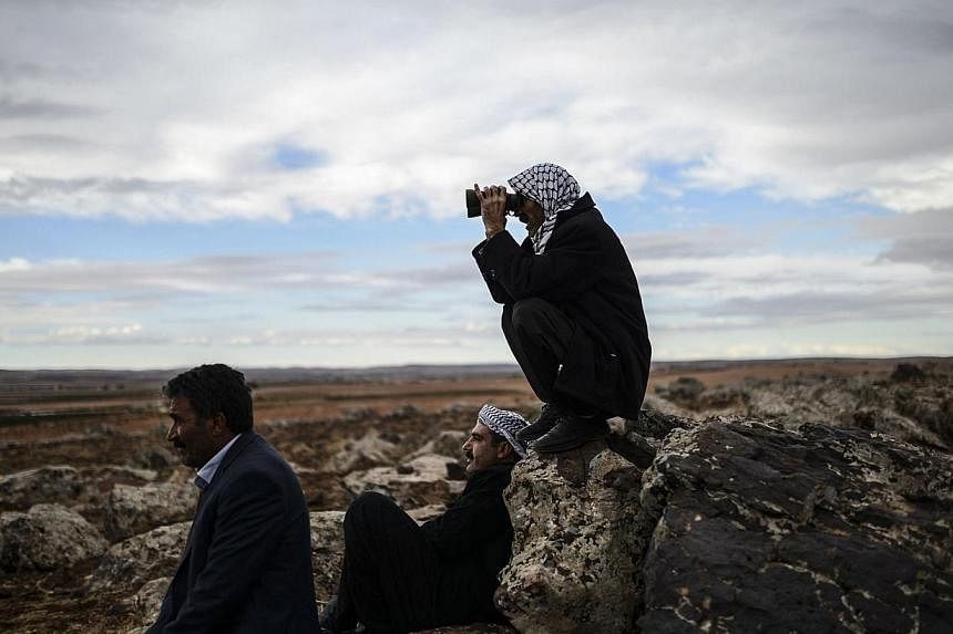 Kurdish people watch the Syrian town of Ain al-Arab, known as Kobane by the Kurds, from the Turkish border in the south-eastern village of Mursitpinar, Sanliurfa province on Oct 19, 2014. -- PHOTO: AFP