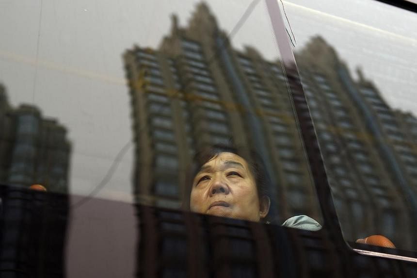 Residential buildings are reflected in a bus window as a passenger looks out, in Beijing on Sept 28, 2014. With a faltering property market increasingly dragging on manufacturing and investment, growth in the world's second-largest economy cooled to 