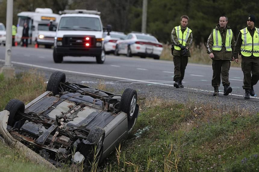 A Surete du Quebec officer investigates an overturned vehicle in Saint-Jean-sur-Richelieu, Quebec, on October 20, 2014. Two Canadian soldiers were injured in a hit-and-run on Monday by a male driver who was later shot dead by police officers. -- PHOT
