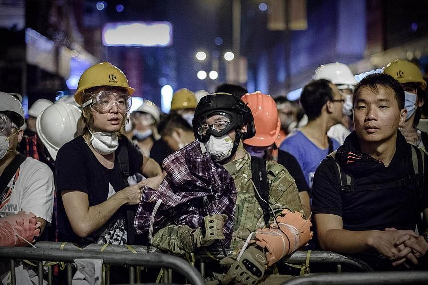 In this picture taken on Oct 19, 2014 pro-democracy protesters wearing protective gear stand at a barricade in the Mongkok district of Hong Kong. &nbsp;-- PHOTO: AFP