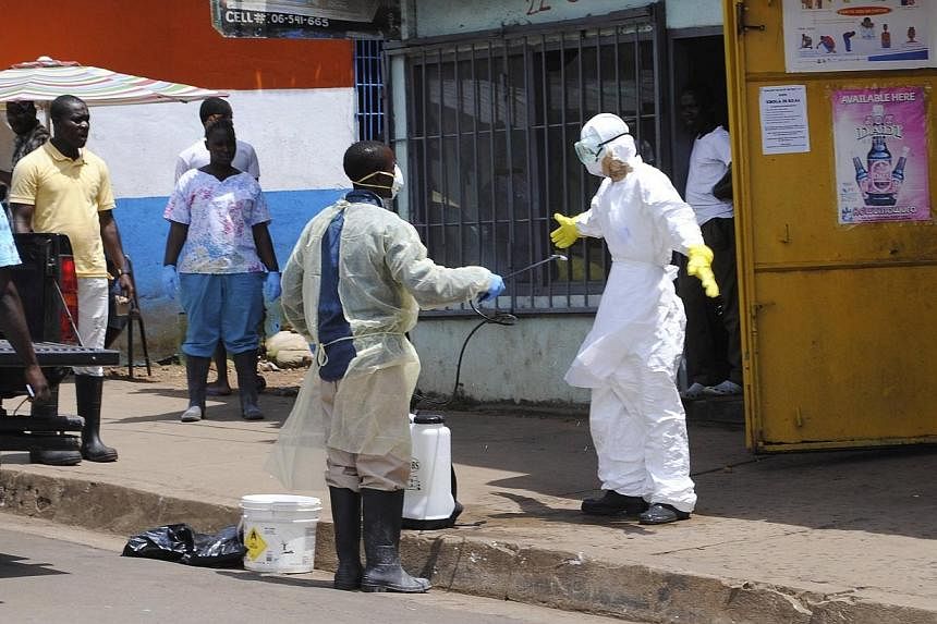 A member of a burial team sprays a colleague with chlorine disinfectant in Monrovia on Oct 20, 2014.&nbsp;Singapore will be making a further contribution of US$150,000 (S$190,575) to the World Health Organisation (WHO) to help fight Ebola. -- PHOTO: 