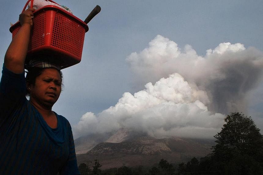 A woman carrying belongings flees from the eruption of Mount Sinabung volcano (background) seen from Karo district on Sumatra island on Oct 14, 2014. -- PHOTO: AFP