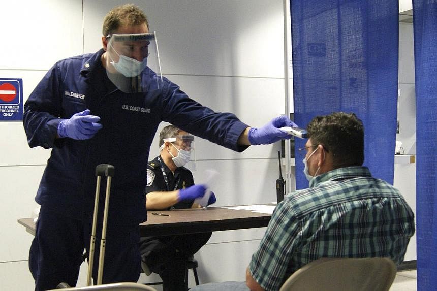 US Coast Guard Health Technician Nathan Wallenmeyer (left) and Customs Border Protection (CBP) Supervisor Sam Ko conduct prescreening measures on a passenger arriving from Sierra Leone at O’Hare International Airport's Terminal 5 in Chicago on Oct 