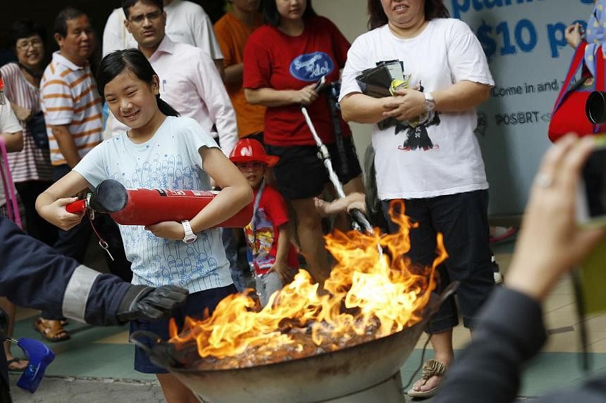 A girl attempts to put out a flaming wok with a fire extinguisher during a SCDF demonstration at the Tanjong Pagar Plaza on Oct 18, 2014. ST PHOTO: DESMOND LUI