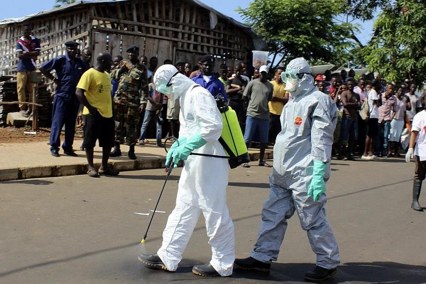 Health workers spray themselves with chlorine disinfectants after removing the body a woman who died of Ebola virus in the Aberdeen district of Freetown, Sierra Leone, on Oct 14, 2014.&nbsp;-- PHOTO: REUTERS