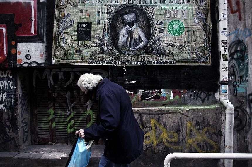An elderly woman walks past graffiti depicting a modified US dollar in Athens on Oct 25, 2014.&nbsp;-- PHOTO: AFP