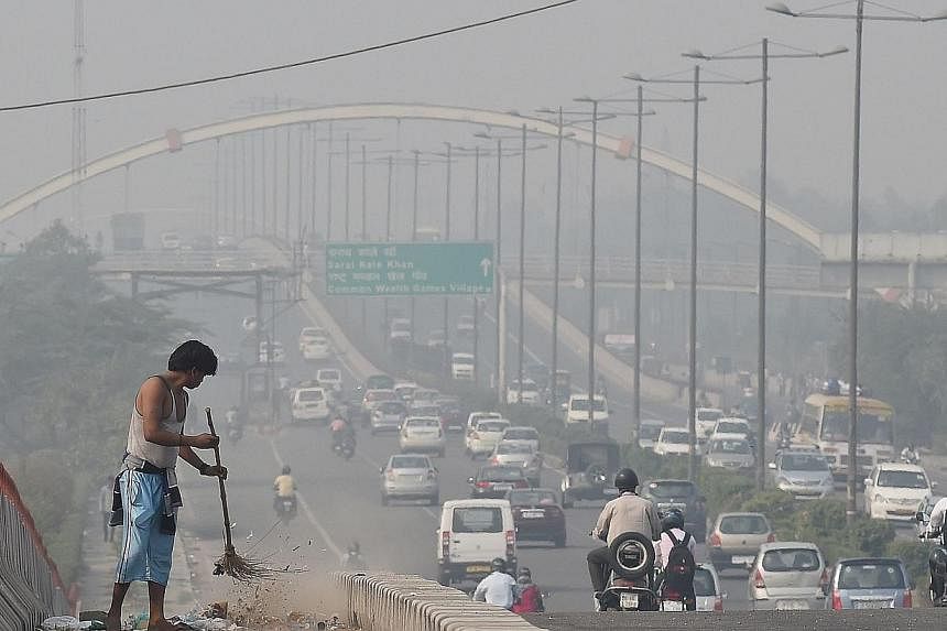 An Indian sweeper cleans a flyover as smog covers the capital's skyline the morning after celebrations for the Diwali festival in New Delhi on Oct 24, 2014. -- PHOTO: AFP&nbsp;