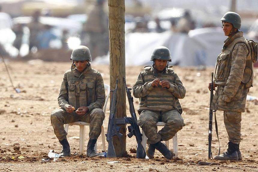 Turkish soldiers stand guard as Syrian Kurdish refugees wait behind the border fences to cross into Turkey near the south-eastern town of Suruc in Sanliurfa province on Oct 17, 2014. -- PHOTO: REUTERS