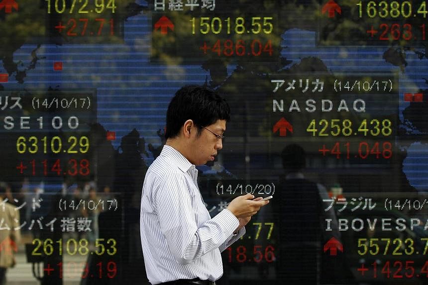 A pedestrian uses his mobile phone as he walks past an electronic board showing the stock market indices of various countries outside a brokerage in Tokyo on Oct 20, 2014. -- PHOTO: REUTERS&nbsp;