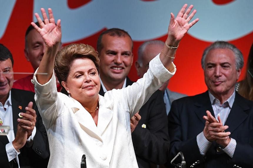 Re-elected Brazilian President Dilma Rousseff (centre) waves next to her Vice-President Michel Temer (right) following her win, in Brasilia on Oct 26, 2014. -- PHOTO: AFP