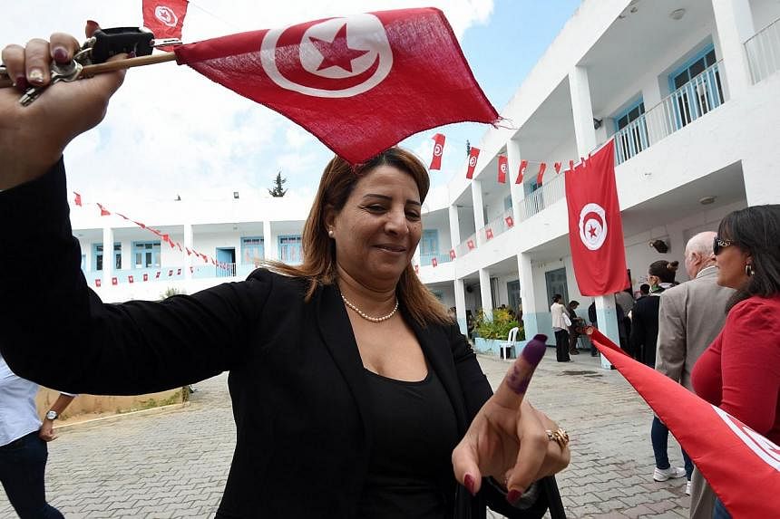 A Tunisian woman shows her ink-stained finger as she waves her national flag after voting in the country's first post-revolution parliamentary election in Ariana, near Tunis, on Oct 26, 2014.&nbsp;Foreign observers on Tuesday praised Tunisia's landma