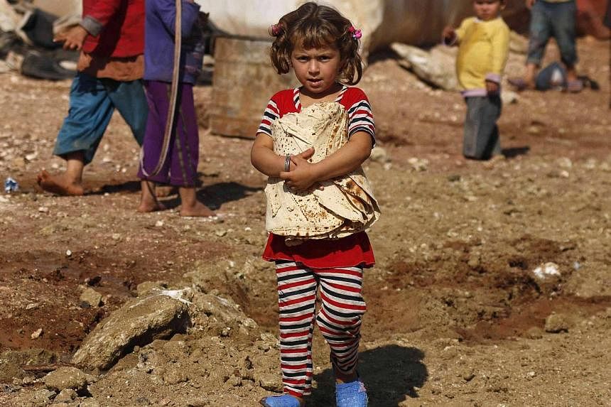 A Syrian refugee girl carries bread as she stands outside tents in the Bab Al-Salam refugee camp in Azaz, near the Syrian-Turkish border. Germany's foreign minister called on Tuesday for a "vow of solidarity" from the international community for mill