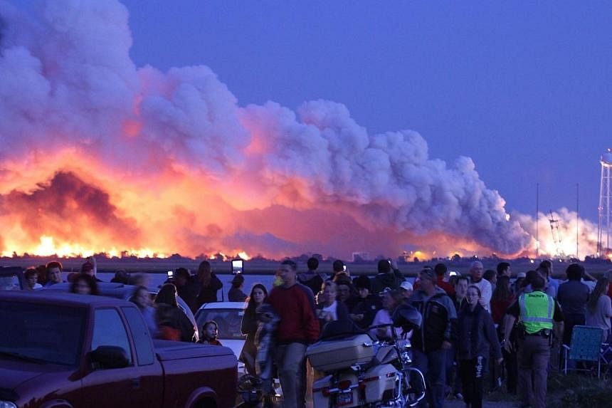 People who came to watch the launch walk away after an unmanned rocket owned by Orbital Sciences Corporation exploded (background) on Oct 28, 2014 just seconds after lift-off from Wallops Island, Virginia, on what was to be a resupply mission to the 
