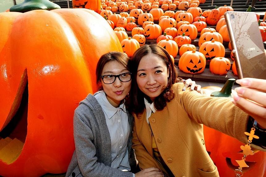 A lady (right) takes a selfie with her friend before an installation of 500 pumpkin lights to mark Halloween in Shenyang, north-east China's Liaoning province on Oct 29, 2014. -- PHOTO: AFP&nbsp;