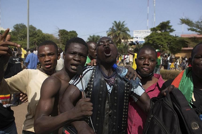 Anti-government protesters shout while holding a microphone used for parliament sessions outside the parliament building in Ouagadougou, capital of Burkina Faso, on Oct 30, 2014. -- PHOTO: REUTERS