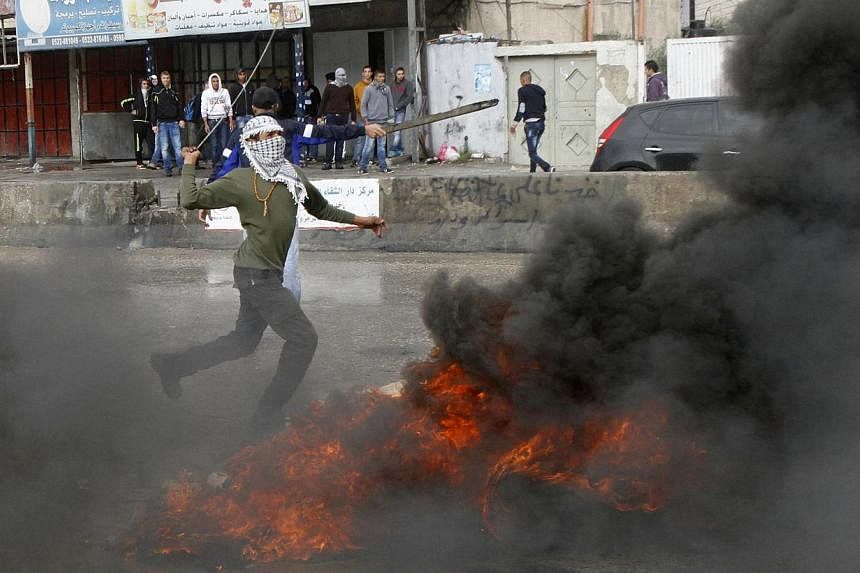 A masked Palestinian protester uses a sling shot to throw stones at Israeli troops, during clashes following an anti-Israel demonstration over the entry restrictions to the Al-Aqsa mosque, at Qalandia checkpoint near the West Bank city of Ramallah Oc