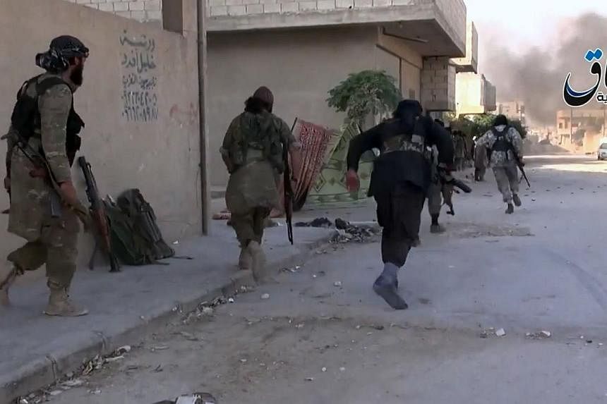 An image grab taken from a video uploaded on Oct 11, 2014, by Aamaq News Agency, a Youtube channel which posts videos from areas under the Islamic State (IS) group's control, allegedly shows an Islamic State group fighters running across a street und