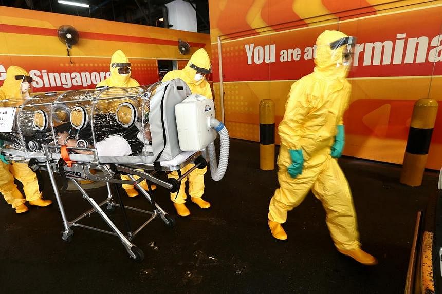 Workers in protective gear attending to a mock Ebola patient, in an exercise to demonstrate Singapore’s defence against highly infectious diseases, at Changi Airport’s Terminal 2 on Aug 14, 2014. -- PHOTO: ZAOBAO