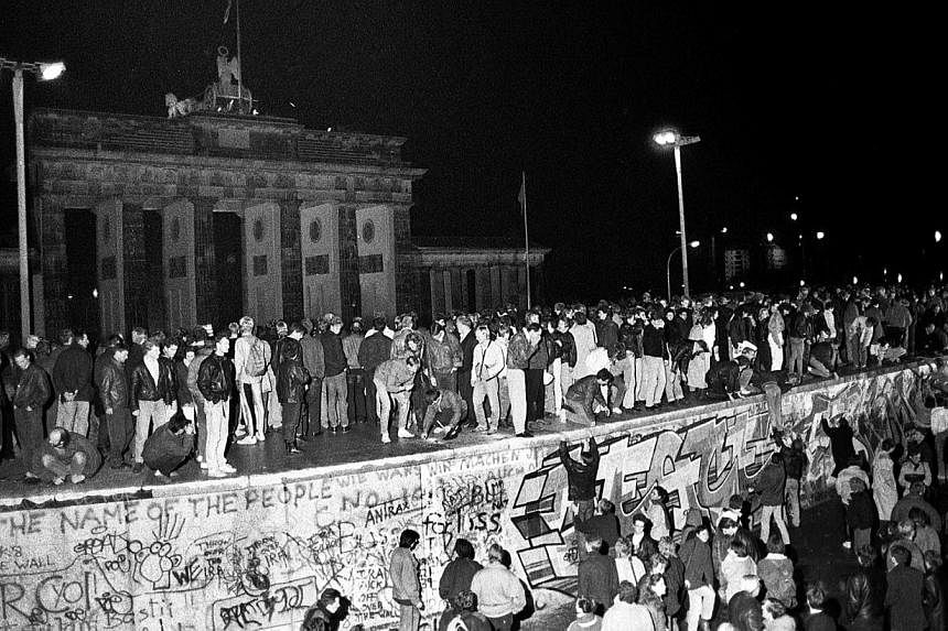 East and West German citizens celebrate as they climb the Berlin wall at the Brandenburg Gate after the opening of the East German border was announced in Berlin, in this file picture taken on Nov 9, 1989. -- PHOTO: REUTERS