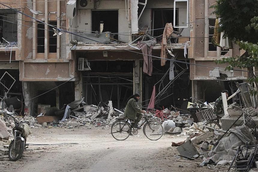 A man rides a bicycle past damaged buildings in the Damascus suburb of Jobar on Oct 28, 2014.&nbsp;Shelling of a rebel-held area in the north-east suburb of Qabun in the Syrian capital killed 13 children on Wednesday, a monitor said revising an earli